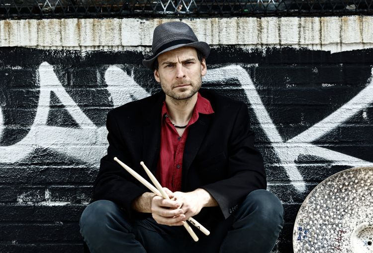 Ari Hoenig holding his drumsticks, in front of a graffiti background